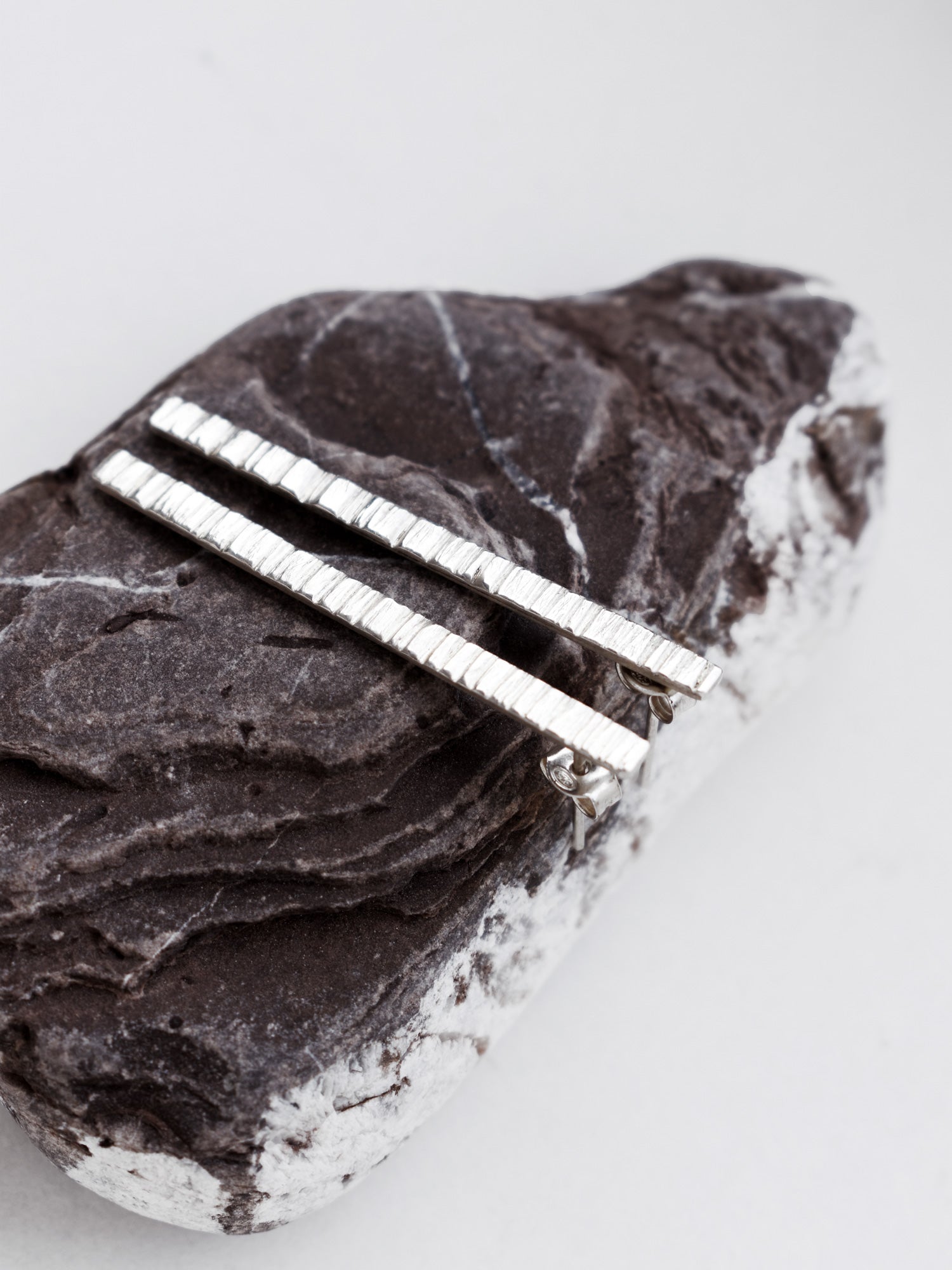 Pair of textured silver bar stud earrings on a textured stone surface