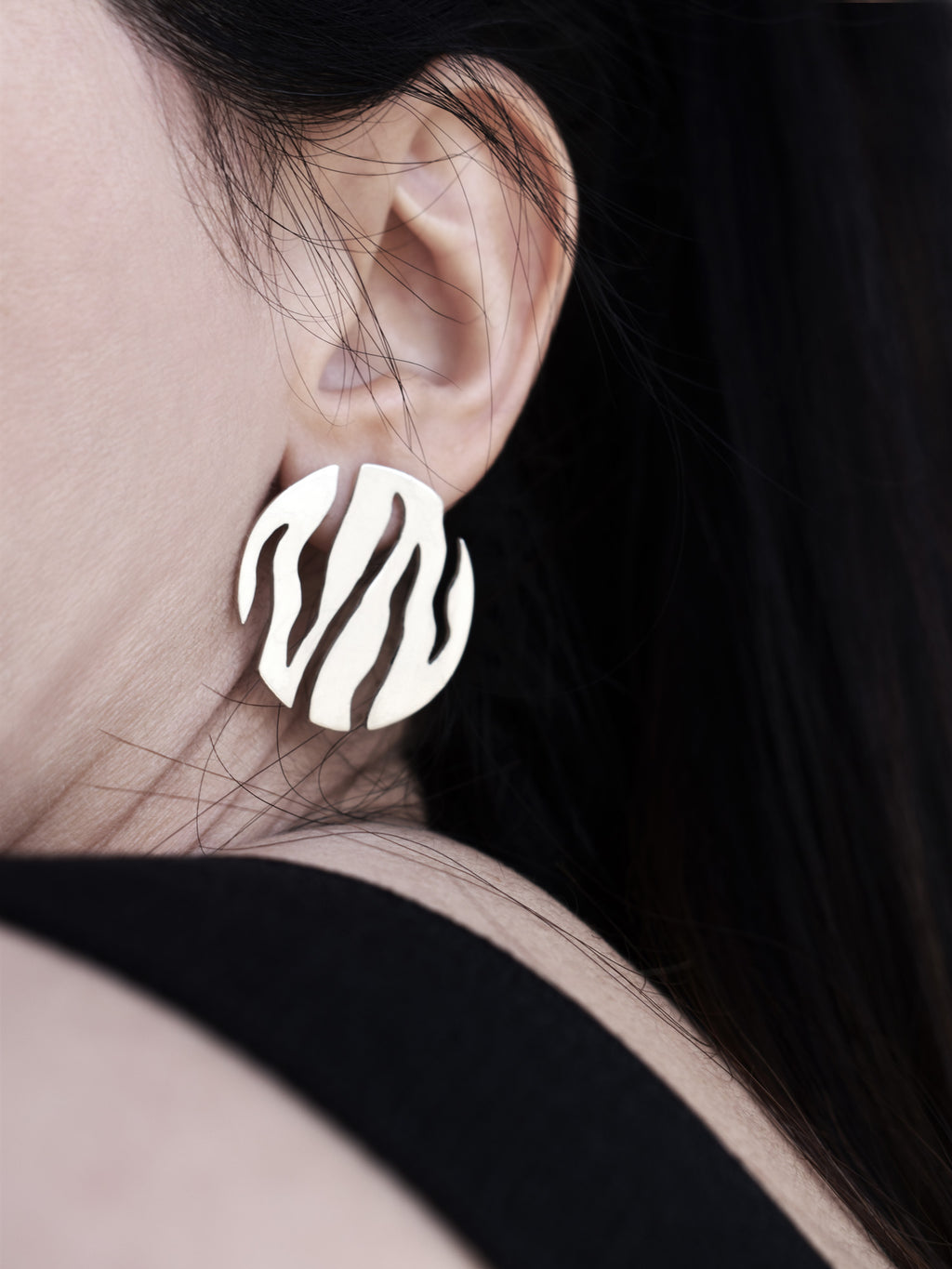 Close-up of a woman wearing a round silver stud earring with flowing cutouts