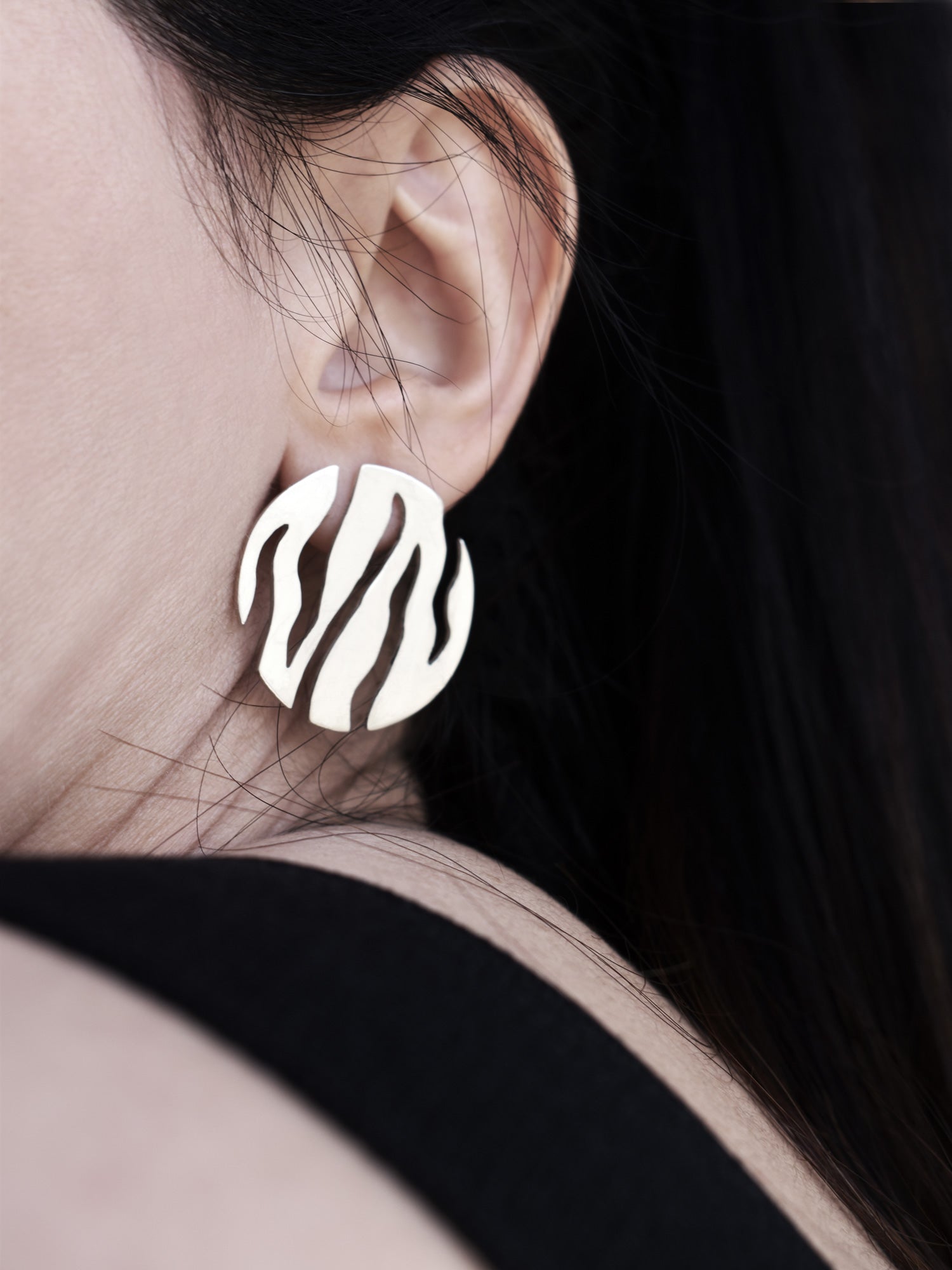 Close-up of a woman wearing a round silver stud earring with flowing cutouts