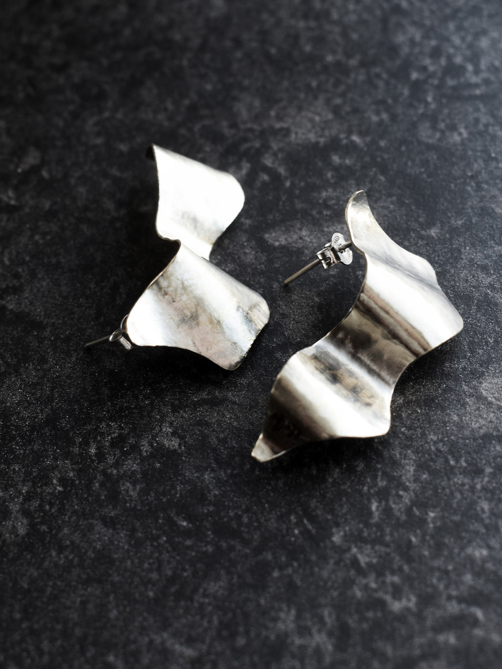 Pair of sculptural silver stud earrings on a black textured background