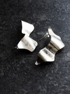Pair of sculptural silver stud earrings on a black textured background