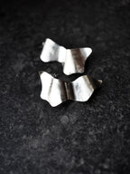 Pair of sculptural silver stud earrings on a black textured background