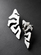 Pair of organic-shaped silver stud earrings with cutout details on a black background
