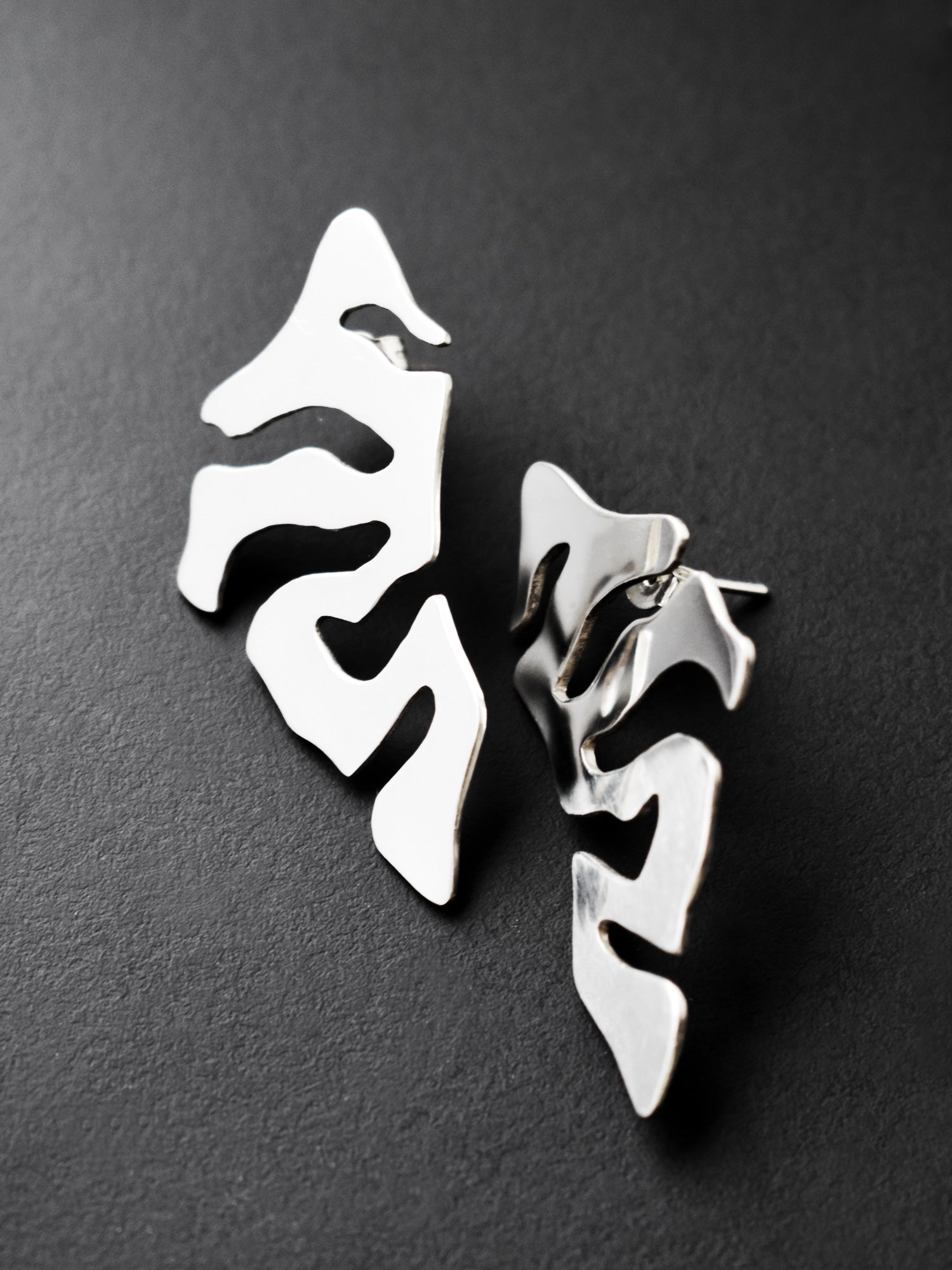 Pair of organic-shaped silver stud earrings with cutout details on a black background