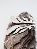 Pair of leaf-shaped silver stud earrings on a textured stone 