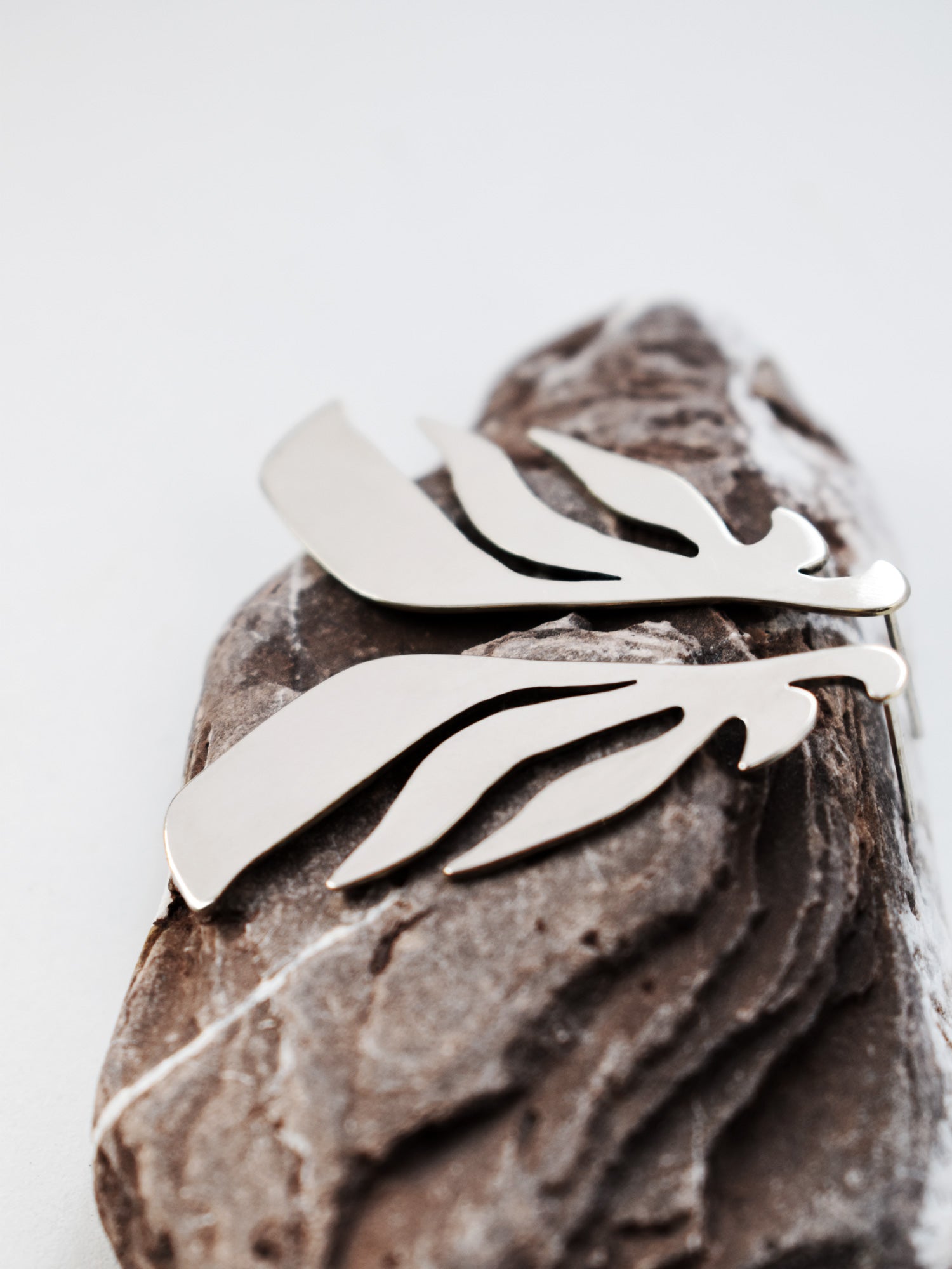 Pair of leaf-shaped silver stud earrings on a textured stone 
