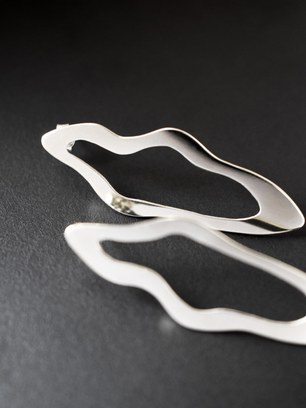Close-up of pair of unique, organic-shaped silver stud earrings on a dark background