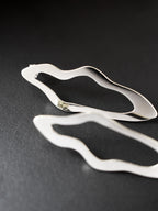 Close-up of pair of unique, organic-shaped silver stud earrings on a dark background