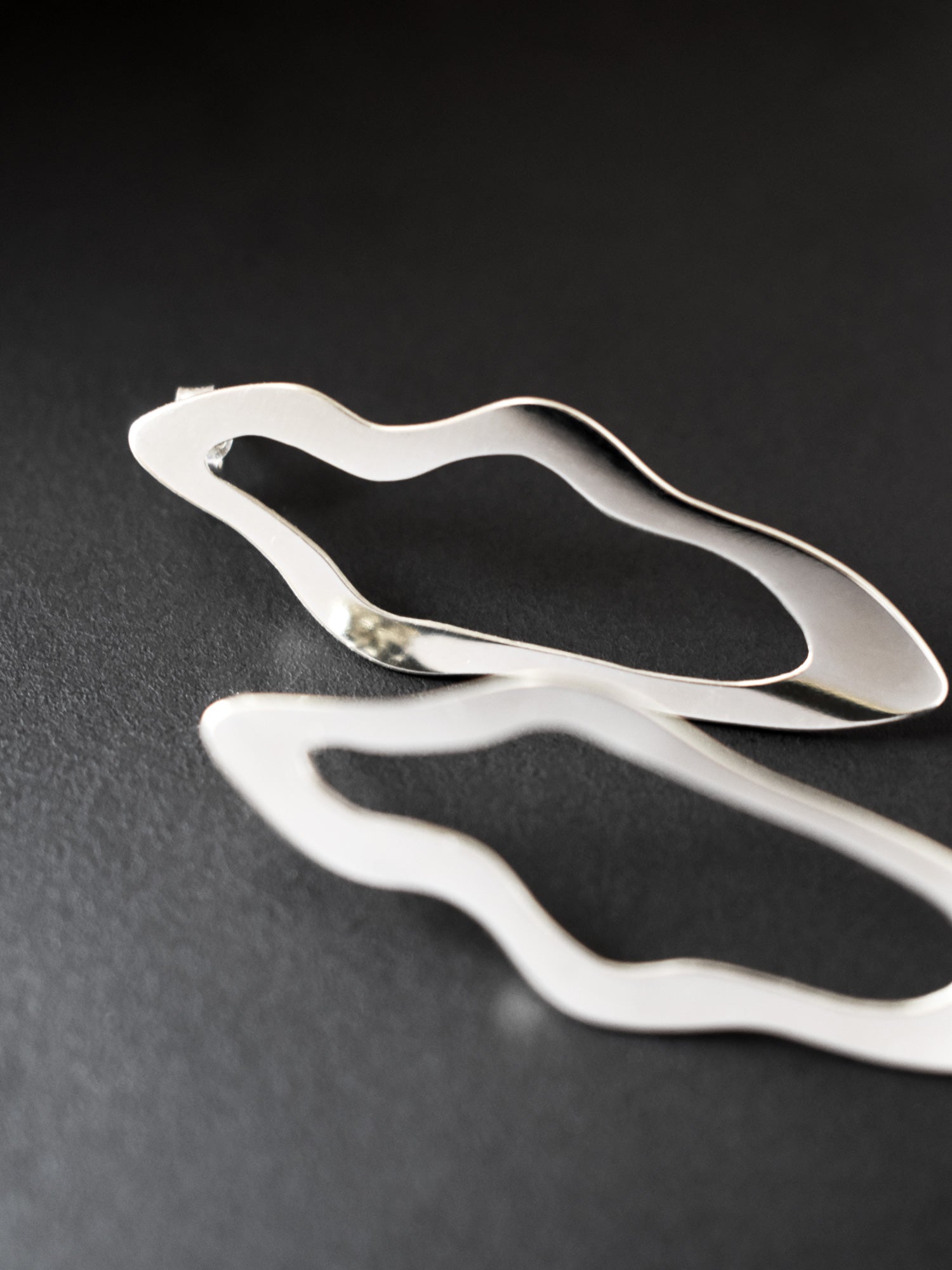 Close-up of pair of unique, organic-shaped silver stud earrings on a dark background