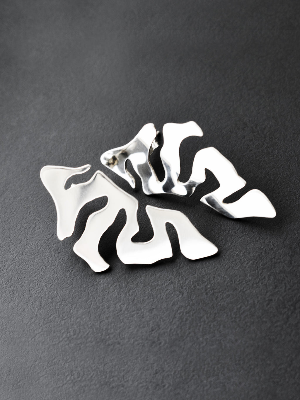 Pair of organic-shaped silver stud earrings with cutout details on a black background