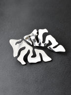 Pair of organic-shaped silver stud earrings with cutout details on a black background