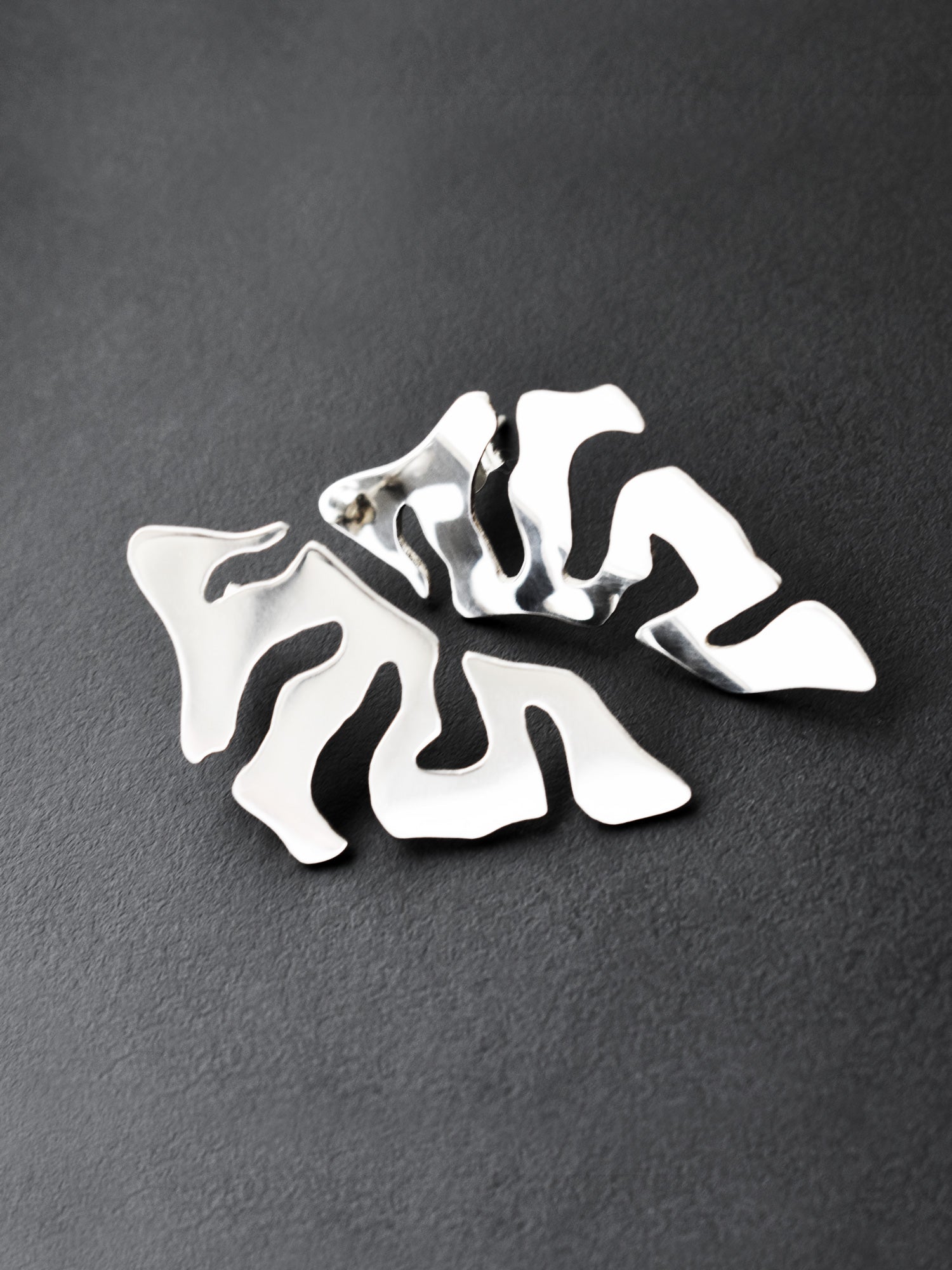 Pair of organic-shaped silver stud earrings with cutout details on a black background