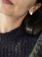 Close-up of a woman wearing a small organic-shaped silver stud earring in a dark sweater