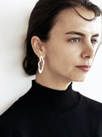 Close-up of a woman wearing a unique, organic-shaped silver stud earring