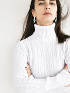 Woman wearing a pair of leaf-shaped silver stud earrings in a white sweater