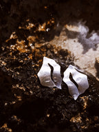 Pair of sculptural silver stud earrings with cutout centers on a textured dark surface