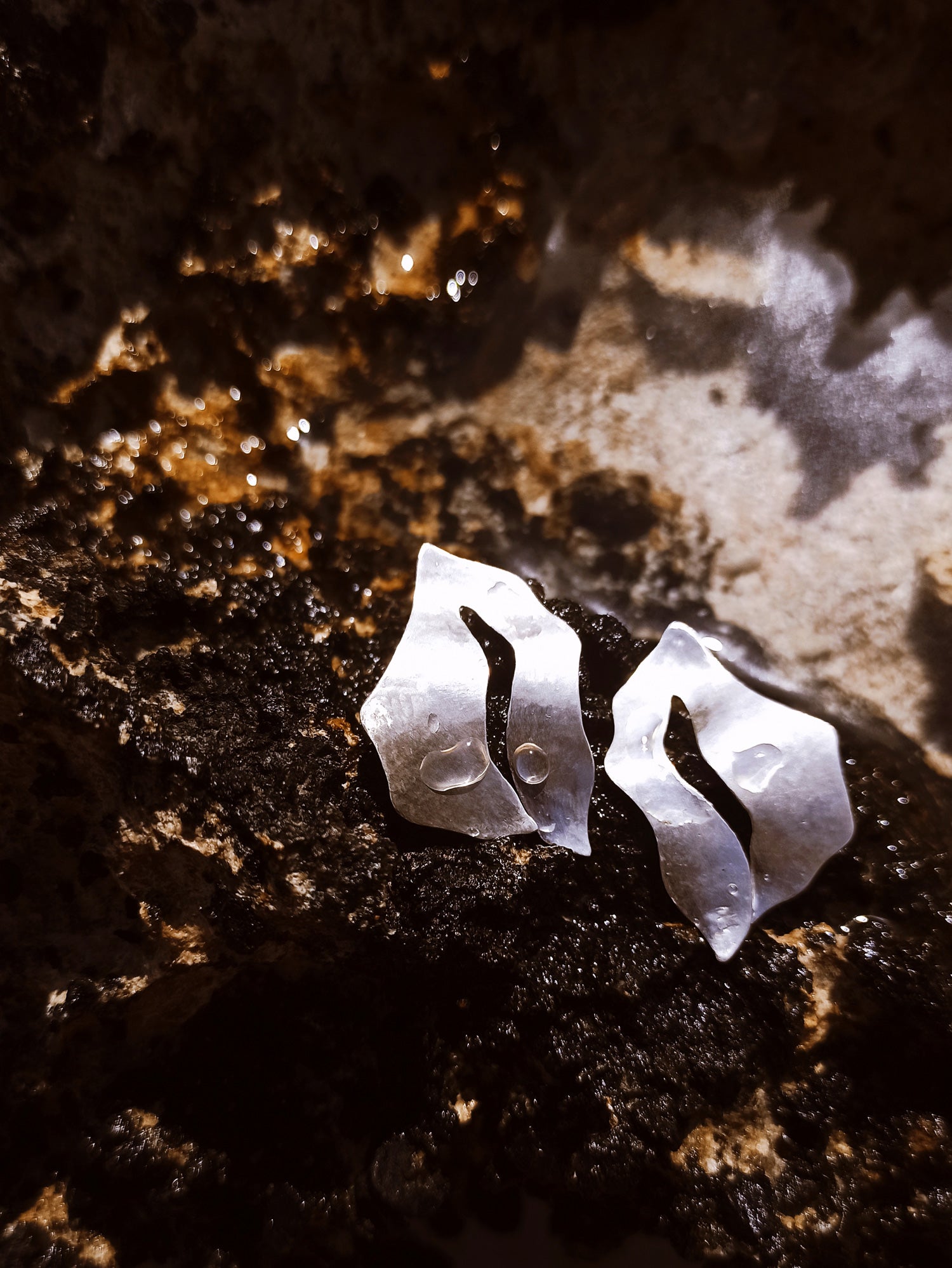 Pair of sculptural silver stud earrings with cutout centers on a textured dark surface