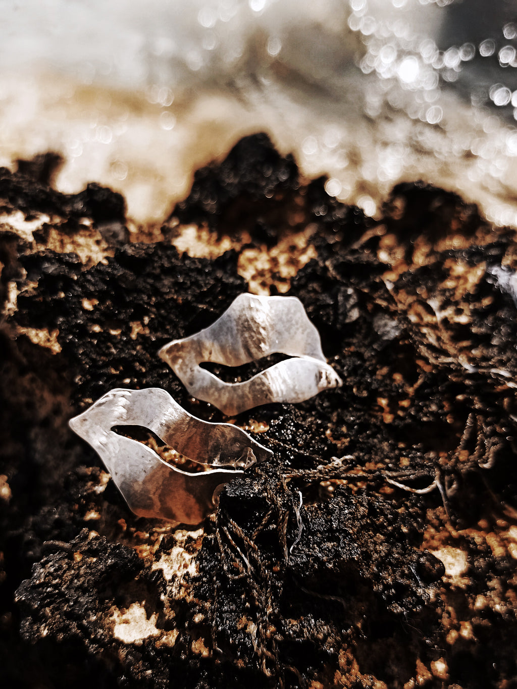 Pair of sculptural silver stud earrings with cutout centers on a textured dark surface
